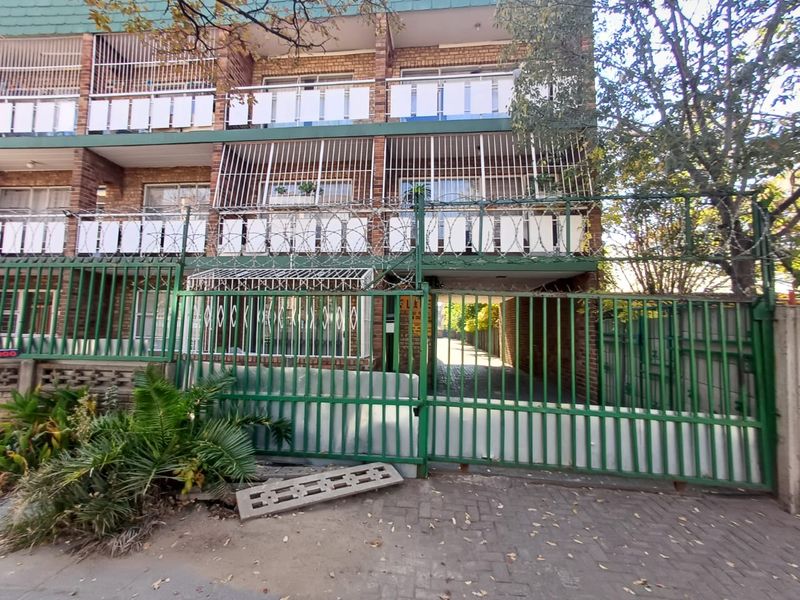 Front exterior view of a multi-story brick apartment building featuring a secure gated entrance, security bars, and balconies.