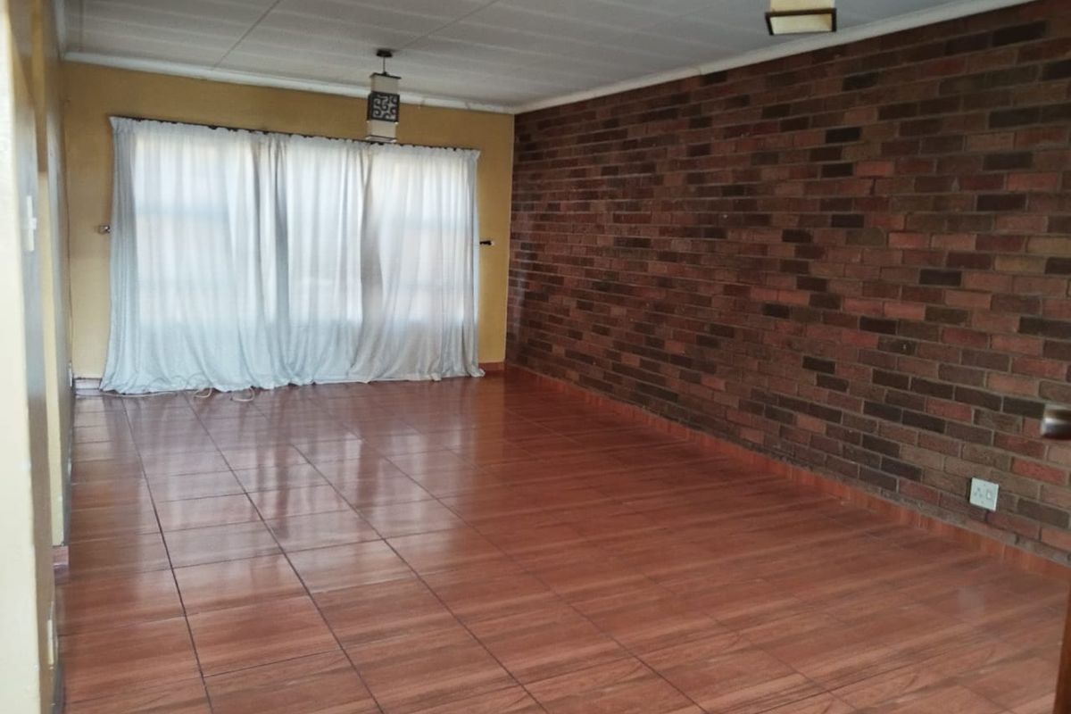 Spacious living area featuring an exposed brick accent wall, tiled flooring, and neutral wall finishes, offering a versatile blank canvas for interior design.