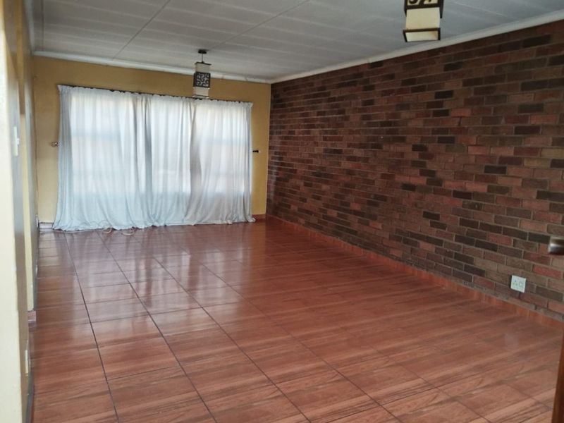 Spacious living area featuring an exposed brick accent wall, tiled flooring, and neutral wall finishes, offering a versatile blank canvas for interior design.