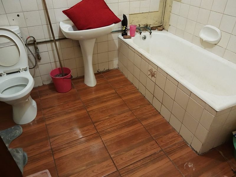 A dated bathroom featuring a pedestal basin, bathtub, and tiled finishes, currently requiring renovation and modernization of fixtures and surfaces.