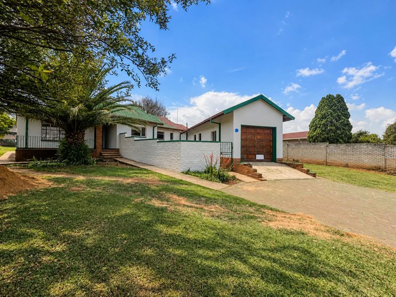 Front exterior view of the property featuring a paved driveway, single garage, and established garden with a brick boundary wall.