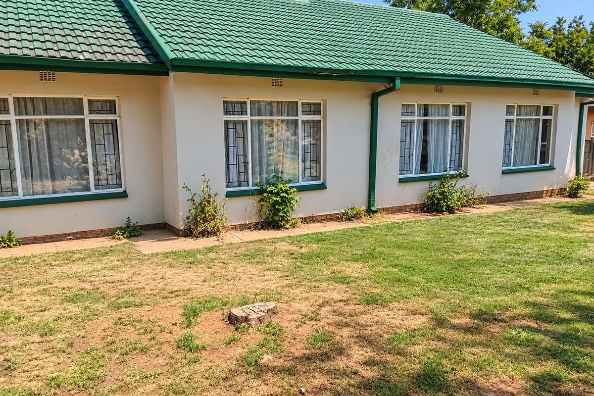Rear view of the house featuring a tiled roof, white exterior walls, and large windows with security bars overlooking a garden area.