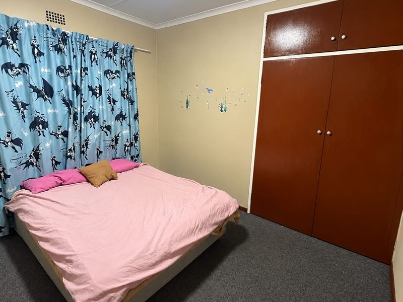 A standard bedroom featuring carpeted flooring, a built-in wardrobe with overhead storage, and a central ceiling light fixture.