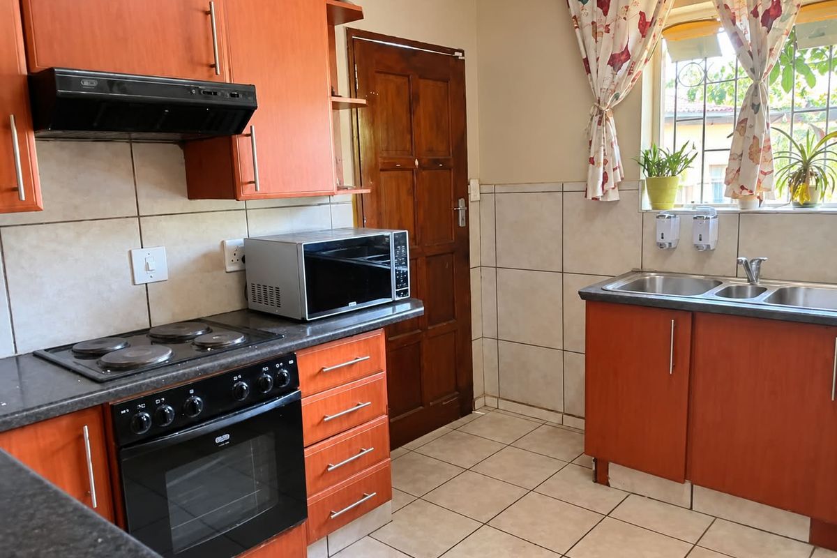 A functional kitchen featuring wooden cabinetry, an electric hob with extractor fan, built-in oven, and a double sink with tiled splashbacks.