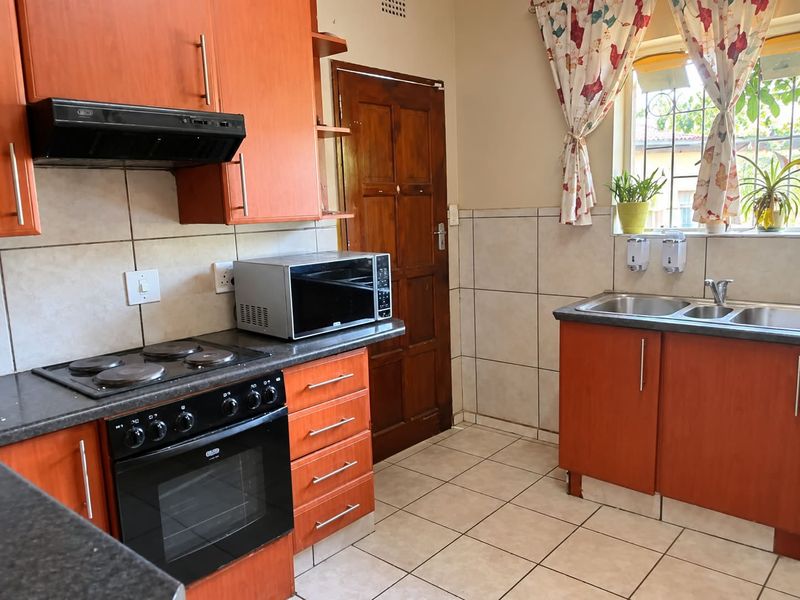 A functional kitchen featuring wooden cabinetry, an electric hob with extractor fan, built-in oven, and a double sink with tiled splashbacks.