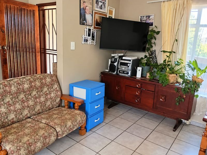 A living room area featuring tiled flooring, a wooden door with a security gate, and neutral wall finishes.