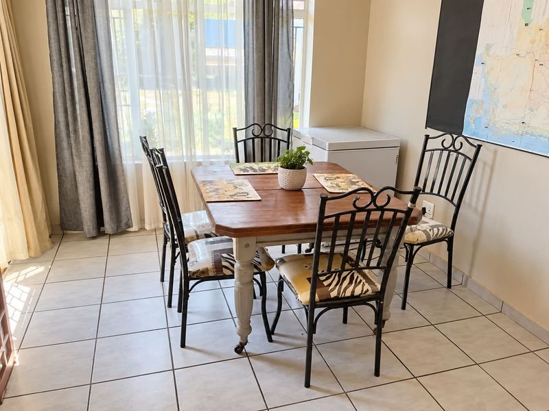 A bright dining area featuring neutral tiled flooring and a large window with curtain treatments, providing a functional space for meals.