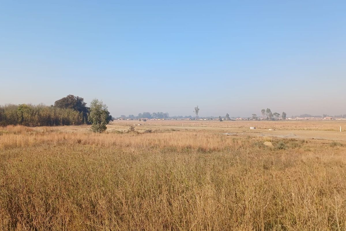 A wide-angle view of a vacant residential plot featuring natural dry grass and open landscape, suitable for future development.