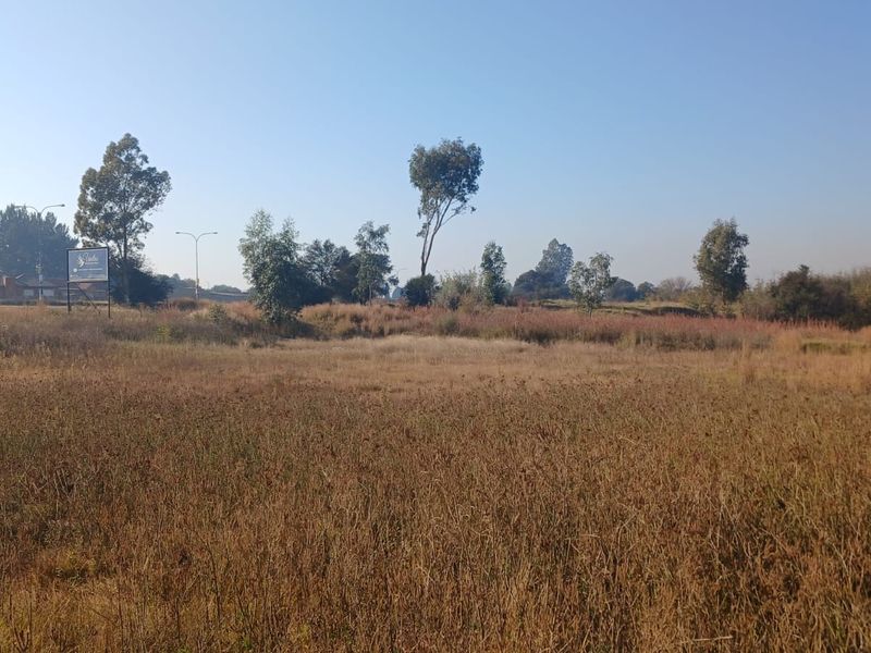A view of a vacant residential plot featuring open grassland and surrounding trees.