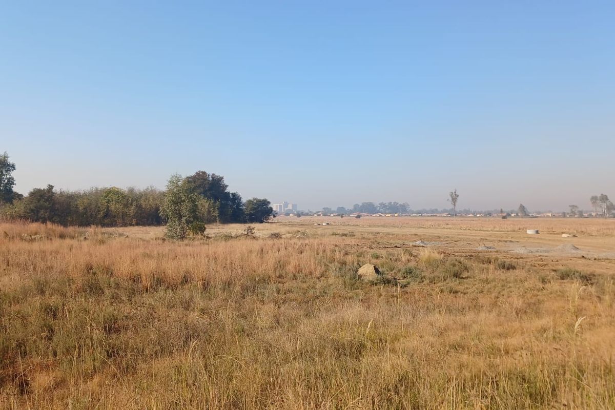 A wide-angle view of a vacant residential plot featuring natural dry grass and open landscape, suitable for future development.