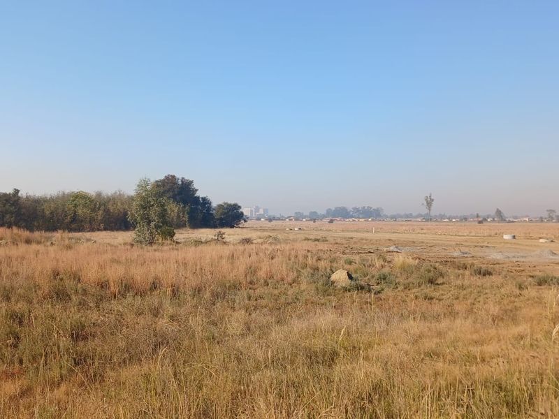A wide-angle view of a vacant residential plot featuring natural dry grass and open landscape, suitable for future development.