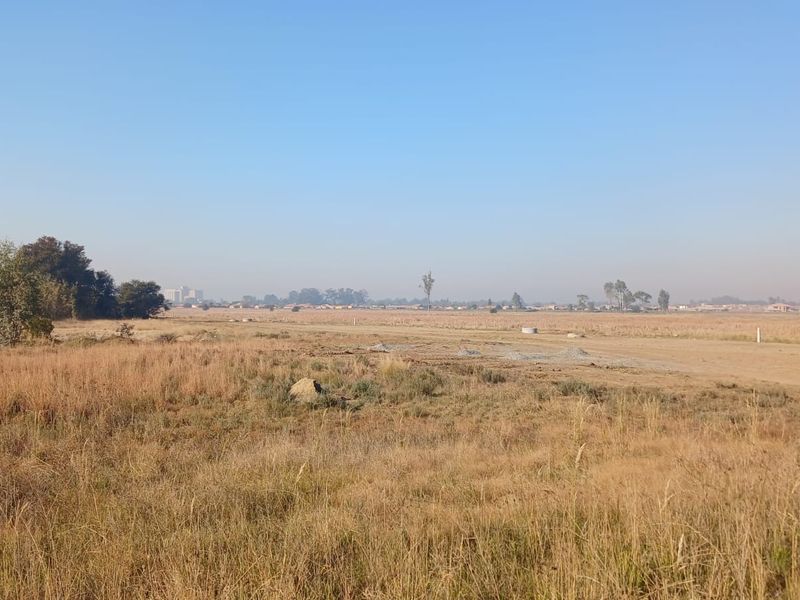 A wide-angle view of a vacant residential plot featuring open grassland and natural terrain, suitable for future development.