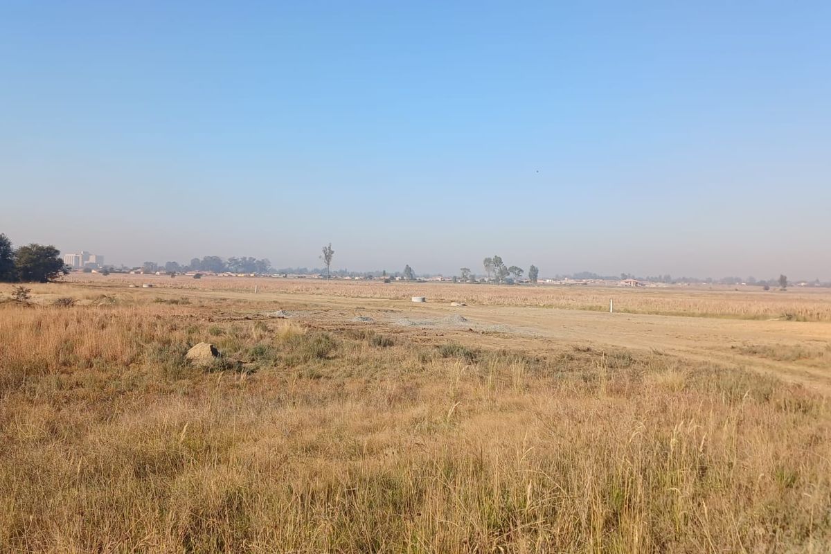 A wide-angle view of a vacant residential plot featuring open grassland and a clear horizon.
