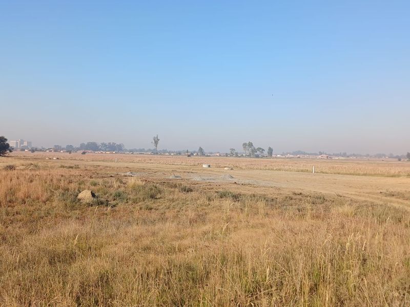 A wide-angle view of a vacant residential plot featuring open grassland and a clear horizon.