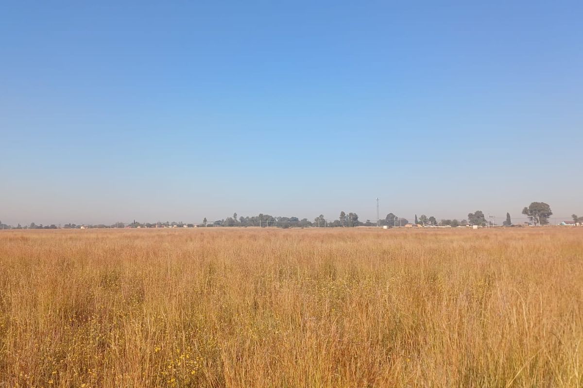 A wide-angle view of a vacant residential plot featuring open, undeveloped grassland under a clear blue sky.
