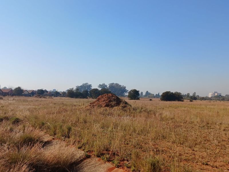 A wide-angle view of a vacant residential plot featuring natural grass cover and level terrain, suitable for future development.