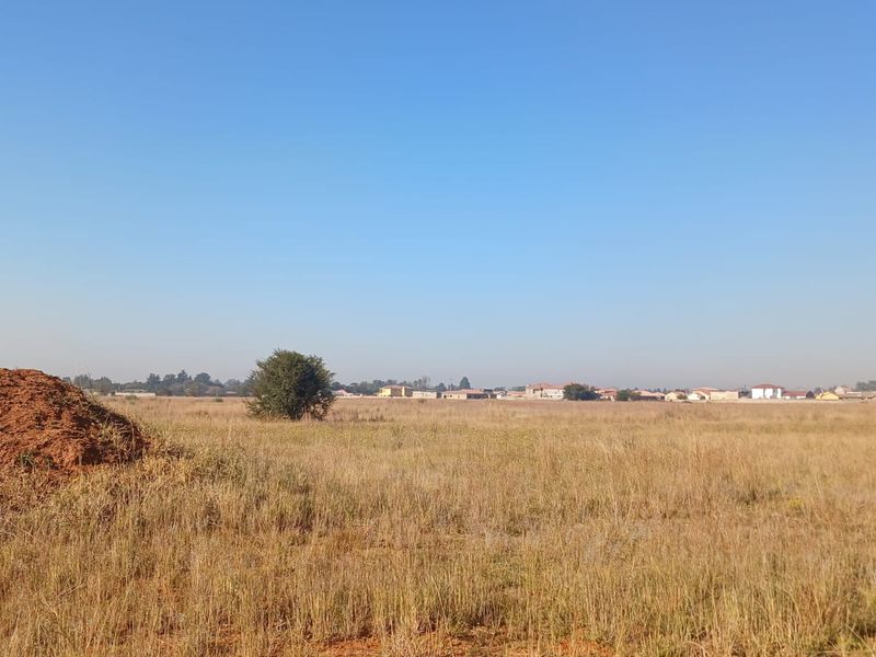 A wide-angle view of a vacant residential plot featuring natural grassland and distant neighborhood views.