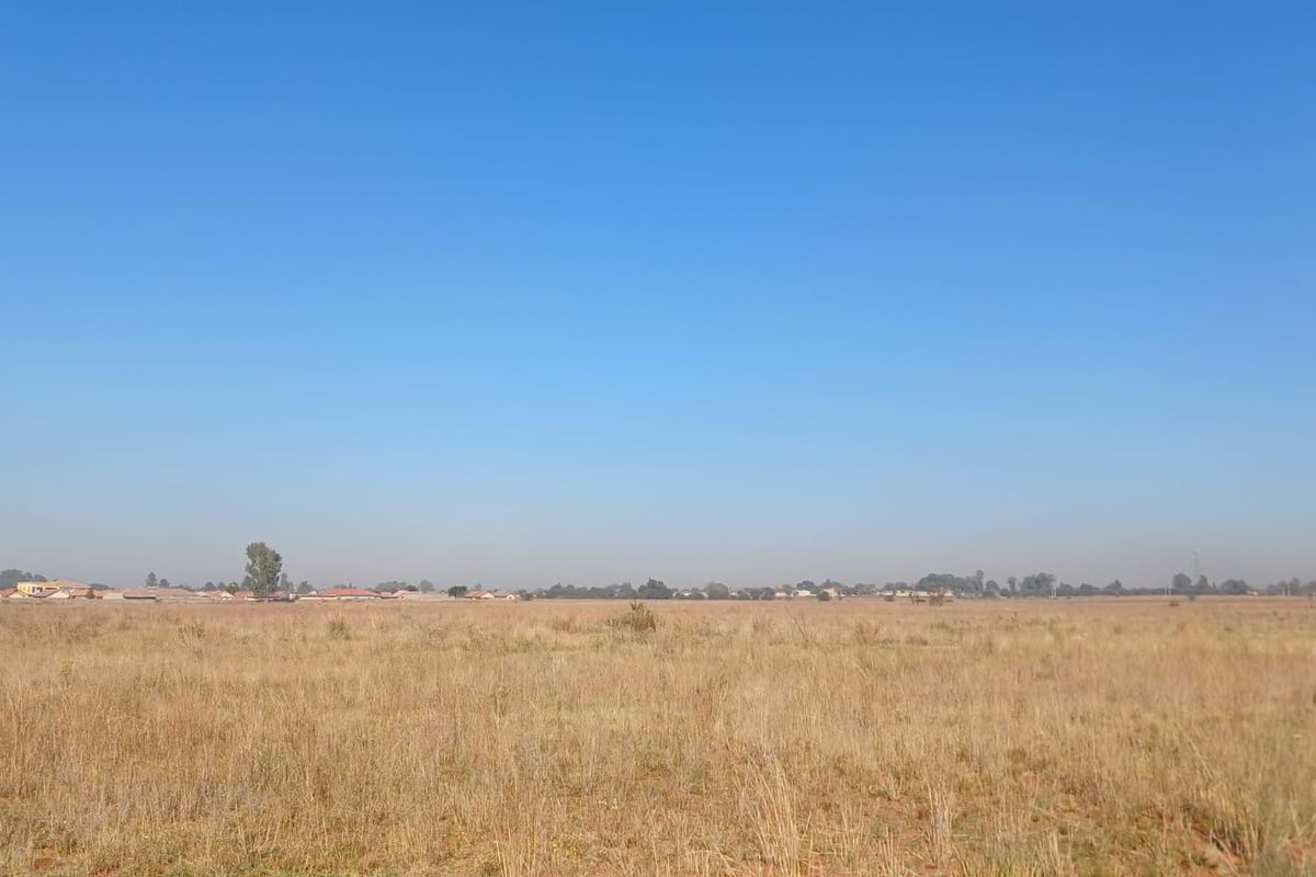 A wide-angle view of a large, flat, vacant residential plot covered in dry grass under a clear blue sky.