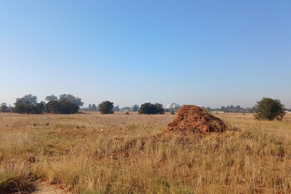 A wide-angle view of a vacant residential plot featuring natural grass cover and scattered trees under a clear blue sky.