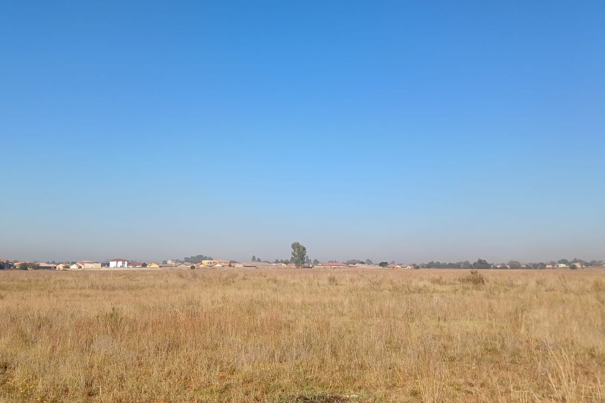 A wide-angle view of a vacant residential plot featuring dry grass and a distant suburban horizon.
