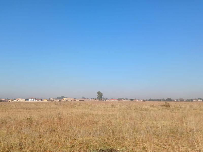 A wide-angle view of a vacant residential plot featuring dry grass and a distant suburban horizon.