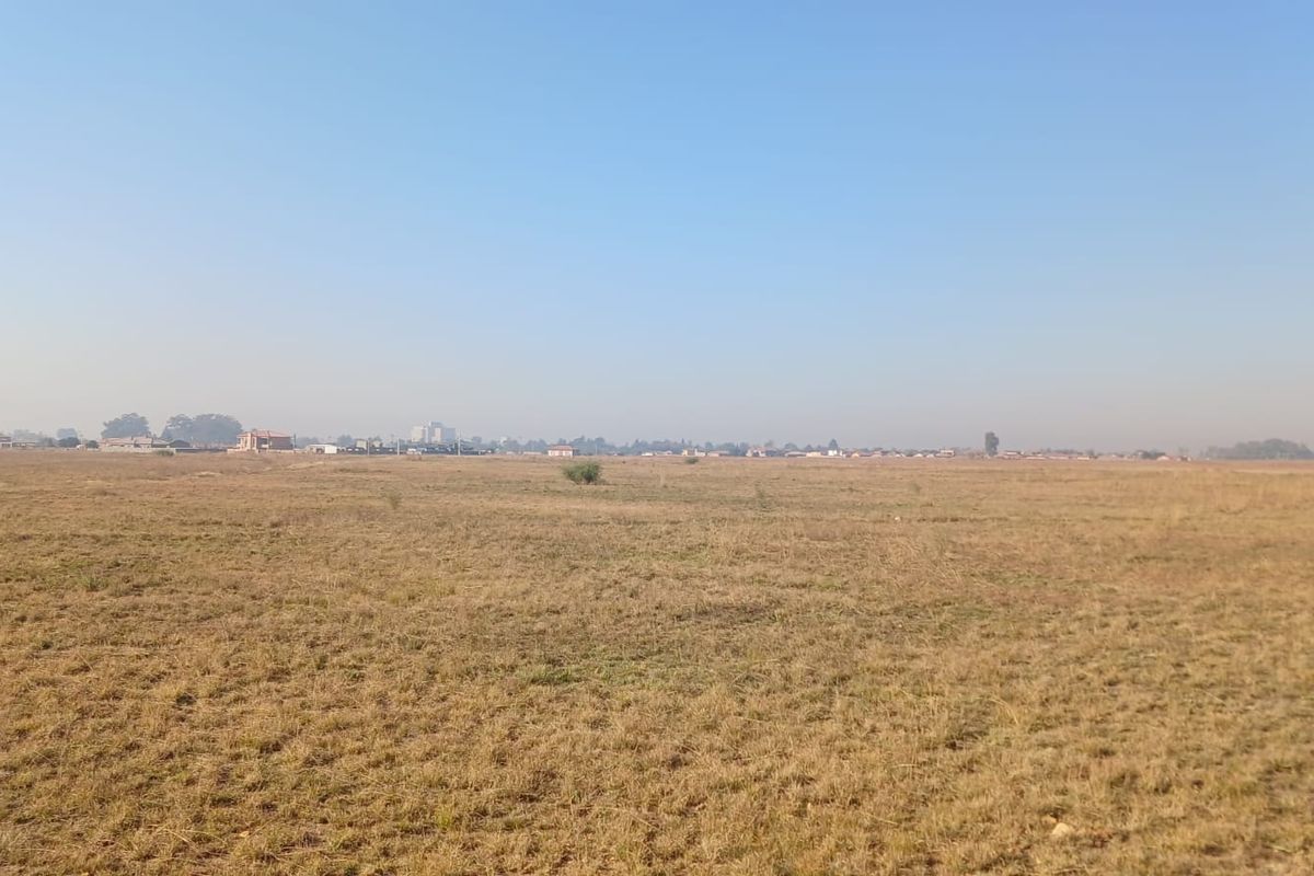 A wide, open expanse of vacant residential land featuring dry grass and a distant view of the surrounding neighborhood.