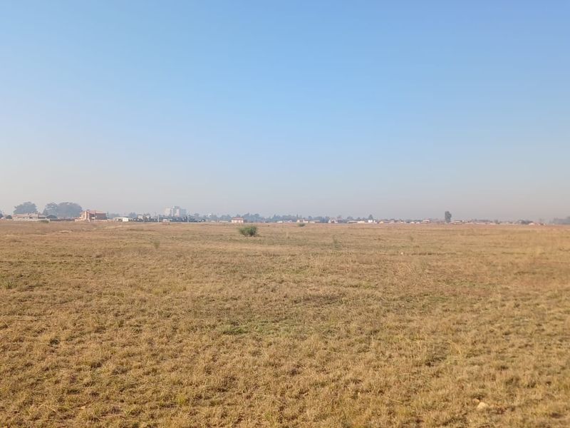A wide, open expanse of vacant residential land featuring dry grass and a distant view of the surrounding neighborhood.