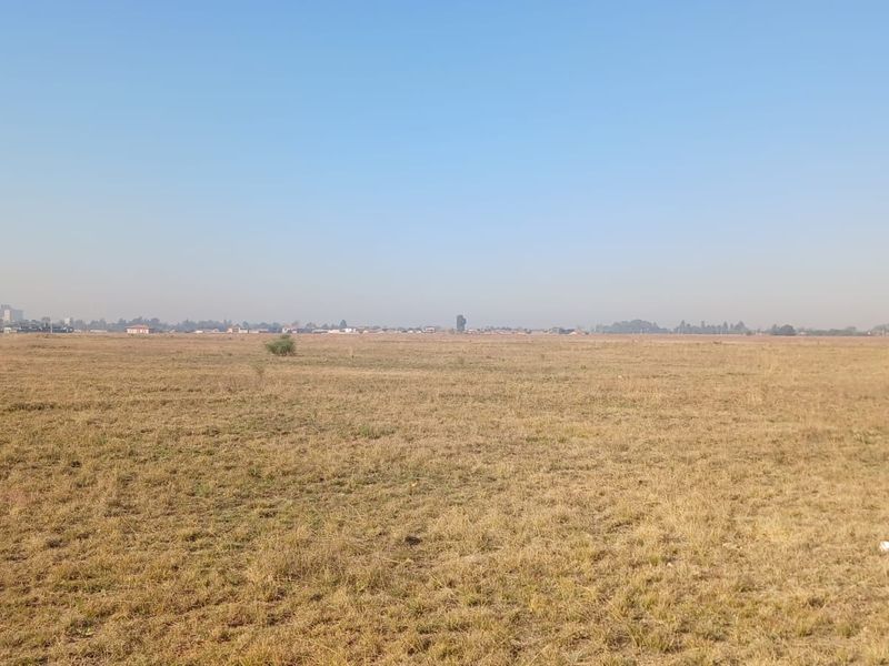 A wide-angle view of a large, flat, undeveloped residential plot of land with dry grass and distant horizon.