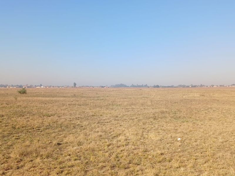A wide, open expanse of vacant residential land featuring dry grass and a clear horizon line.