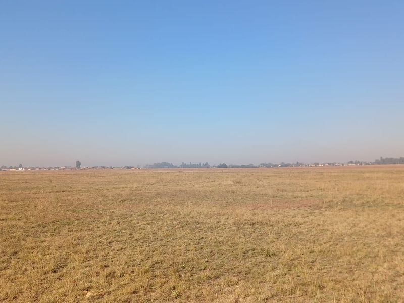A wide, open expanse of vacant residential land featuring flat, grassy terrain under a clear sky.