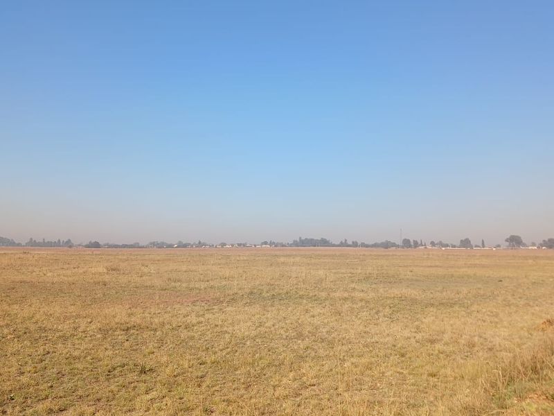 A wide, open expanse of vacant residential land featuring flat, grassy terrain under a clear blue sky.