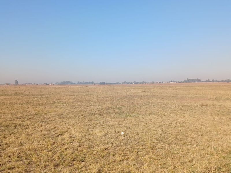 A wide, open expanse of vacant residential land featuring flat, grassy terrain under a clear sky.