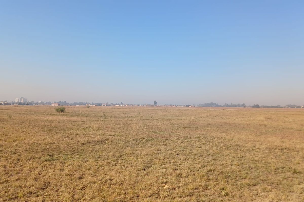 A wide, open expanse of vacant residential land featuring dry grass and a distant horizon view.