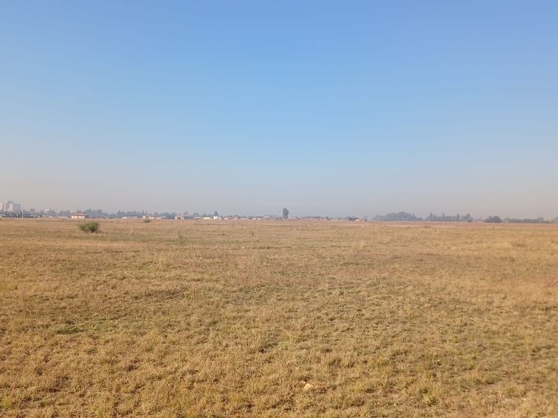 A wide, open expanse of vacant residential land featuring dry grass and a distant horizon view.