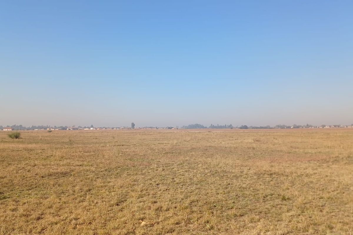 A wide, open expanse of vacant residential land featuring dry grass and a clear horizon line.