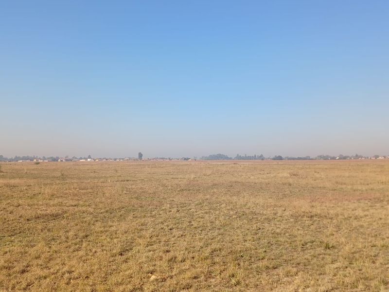 A wide, open expanse of vacant residential land featuring dry grass and a clear horizon line.