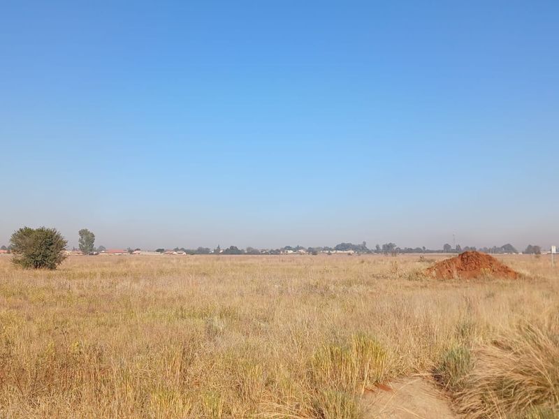 A wide-angle view of a vacant residential plot featuring natural grass cover and open space, suitable for future development.