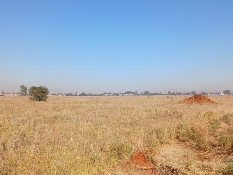 A wide-angle view of a vacant residential plot featuring natural grassland and level terrain, suitable for future development.