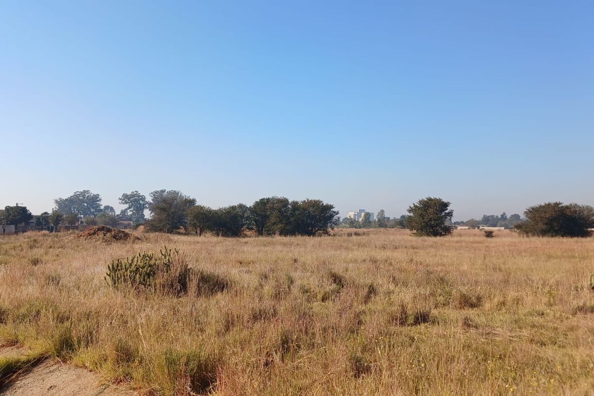 A wide-angle view of a vacant residential plot featuring natural grass and scattered trees, offering a blank canvas for future development.