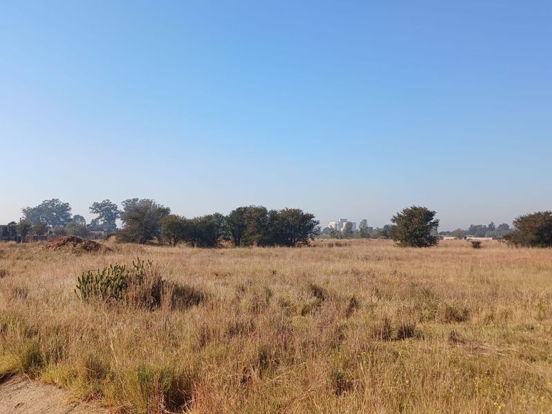 A wide-angle view of a vacant residential plot featuring natural grass and scattered trees, offering a blank canvas for future development.