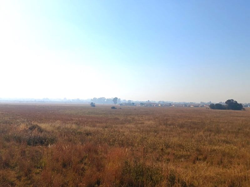 A wide-angle view of an expansive, undeveloped residential land plot featuring natural grassland and distant horizon.