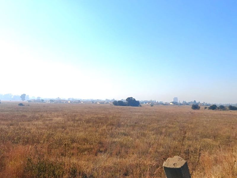 A wide-angle view of a large, undeveloped residential plot featuring dry grassland and distant neighborhood scenery.