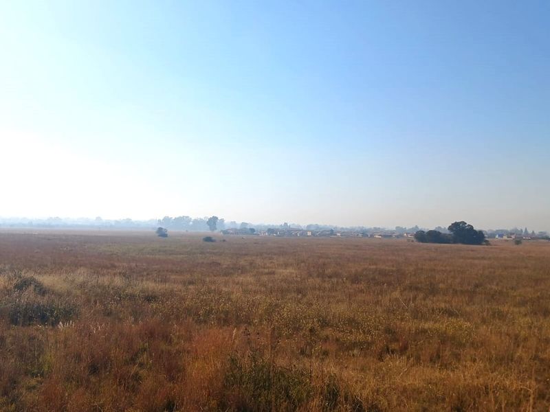 A wide-angle view of an expansive, undeveloped residential land plot featuring natural grassland and distant horizon.