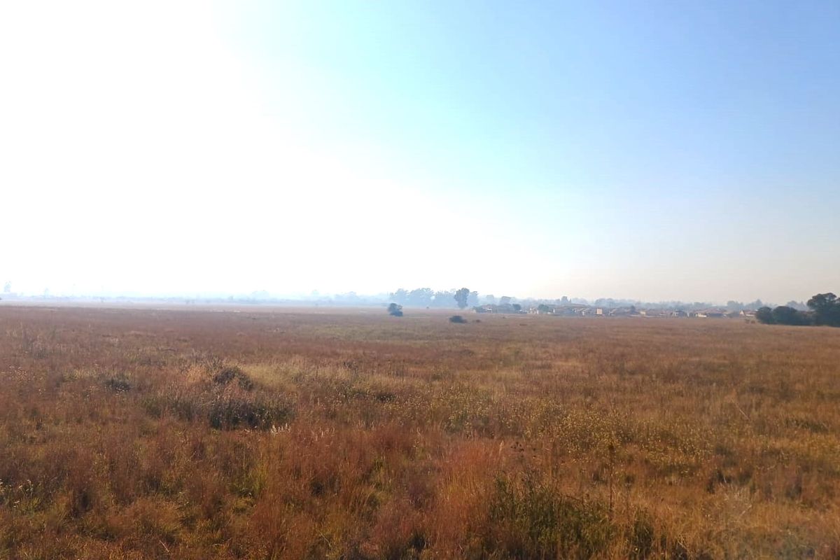 A wide, open expanse of undeveloped residential land featuring natural grassland and distant horizon views.