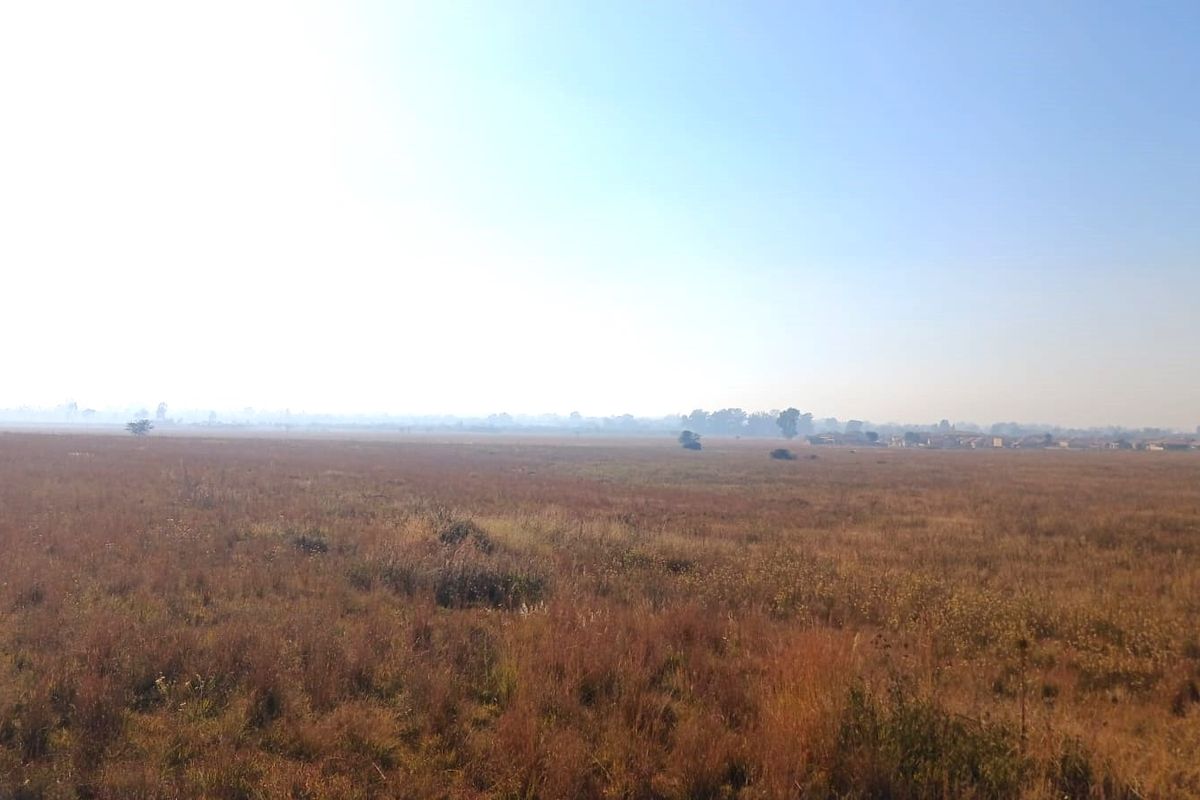 A wide, open expanse of undeveloped residential land featuring natural dry grassland under a clear sky.