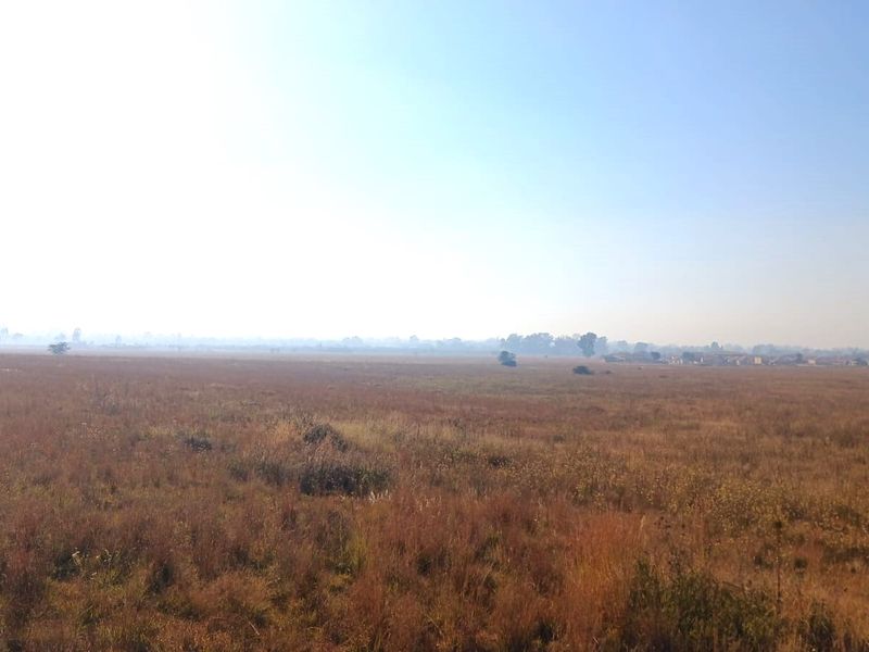 A wide, open expanse of undeveloped residential land featuring natural dry grassland under a clear sky.