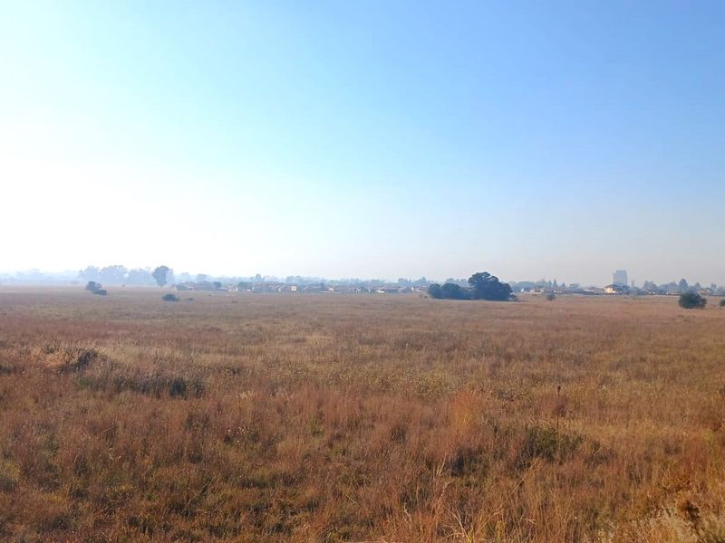A wide-angle view of an expansive, undeveloped residential plot featuring open grassland and a distant horizon.