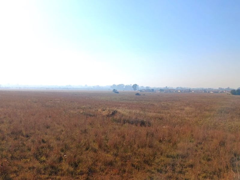 A wide-angle view of an expansive, undeveloped residential land plot featuring natural grassland and distant horizon.