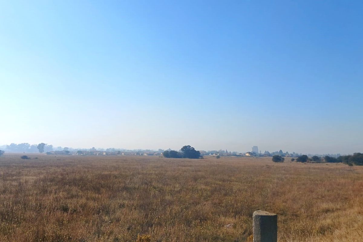 A wide-angle view of an expansive, undeveloped residential land plot featuring dry grassland and distant horizon scenery.