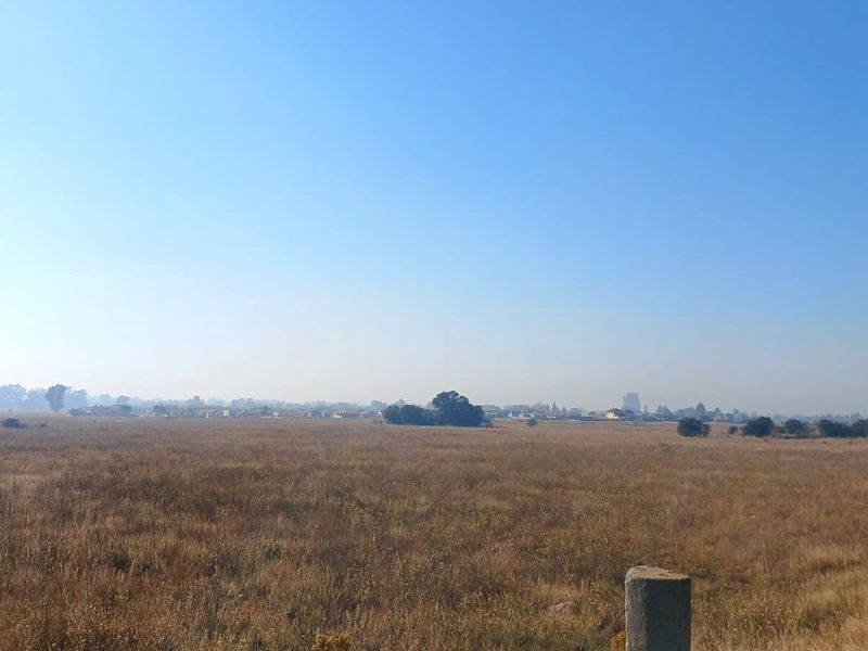 A wide-angle view of an expansive, undeveloped residential land plot featuring dry grassland and distant horizon scenery.